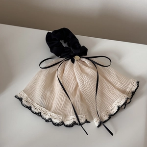 Detail of beige tulle scrunchie featuring black lace trim and golden bow accent