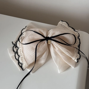 Detail of beige chiffon hair tie with black lace trim and golden pendant decor