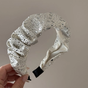 Detail of a beige velvet headband featuring heavy rhinestone embellishments and pleats