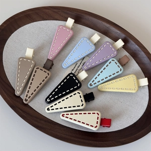 Matte candy-colored triangle hair clips with stitched details in a wooden tray