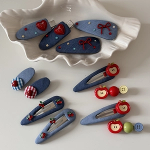 Detail of denim blue hair clips with red heart and apple charms in a shell tray