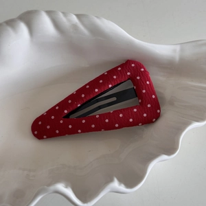 Détail d'une pince à cheveux triangulaire à pois rouges sur un plat en céramique