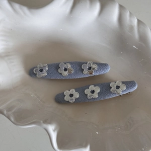 Close-up of blue fabric hair clips with silver flowers on a ceramic shell plate