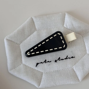 Close-up of a triangular black hair clip with white stitching details on a quilted mat