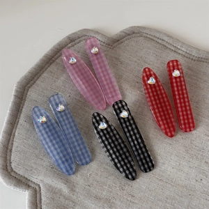 Détail du lot de barrettes à carreaux avec strass en cœur sur un tapis de tissu
