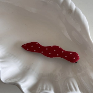 Détail d'une pince à cheveux rouge ondulée à pois blancs dans un bol décoratif en coquille