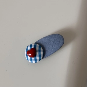 Detailed view of a denim fabric hair clip with a blue checkered button and red heart
