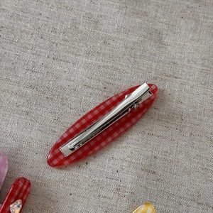 Détail d'une pince à cheveux à carreaux rouges et blancs avec clip crocodile en métal