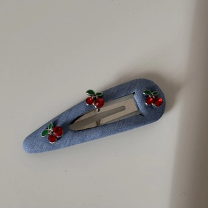 Close-up of blue denim hair clip with red rhinestone cherry pattern and silver metal base