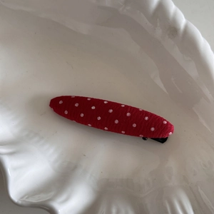 Vue détaillée d'une pince à cheveux rouge à pois sur un plateau en céramique blanche