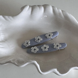 Detail view of two purple fabric hair clips with floral accents on a textured tray