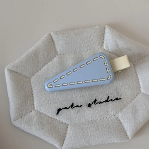 Close-up of light blue triangle hair clip with white stitching on a quilted background