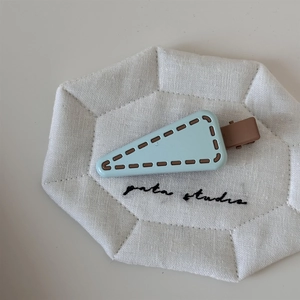 Close-up of light blue triangular hair clip with brown stitching details on linen mat