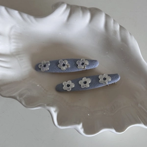 Close-up of light blue denim hair clips with silver hollowed flower accents on a shell tray