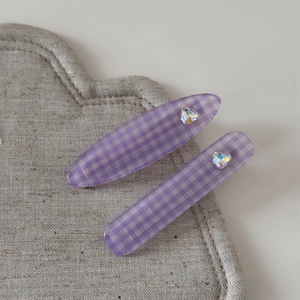 Détail de deux barrettes à carreaux violets avec strass en cœur sur un tapis de lin