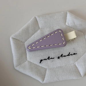 Close-up of a light purple triangular hair clip with white stitching detail on a fabric pad