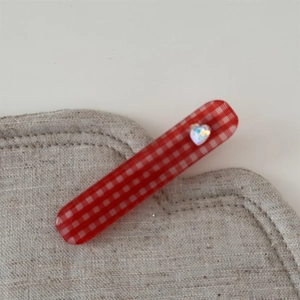 Détail de la pince à cheveux vichy rouge avec cœur iridescent sur fond en lin texturé