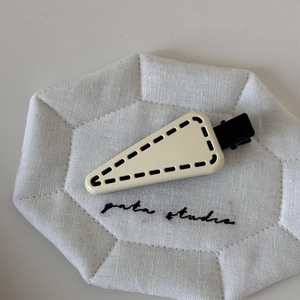 Detail of cream-colored triangle hair clip with decorative black stitching on fabric tray