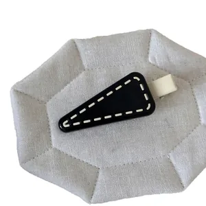 Black triangle hair clip with white stitching on a decorative fabric pad for women