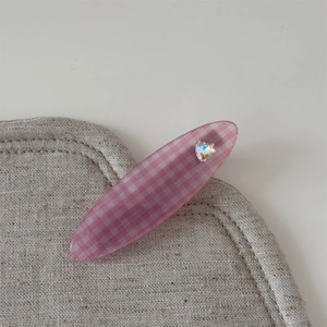 Gros plan d'une pince à cheveux rose à carreaux avec cristal cœur sur du lin