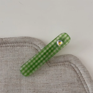 Détail d'une pince à cheveux à carreaux verts avec cristal en forme de cœur sur lin