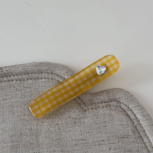 Détail d'une pince à cheveux à carreaux jaunes avec un strass en forme de cœur