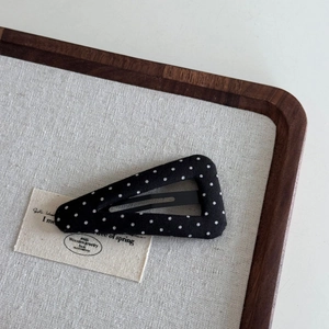 Detail of triangular black hair clip with white polka dots on a linen display tray
