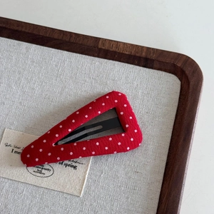 Detail of red fabric hair clip with white polka dots and metal snap base on linen