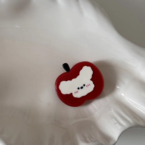 Vue détaillée d'une pince à cheveux pomme rouge en acétate avec motif chiot blanc sur plateau