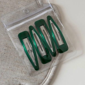 Detail of four dark green marble-textured BB hair clips in a transparent zip bag