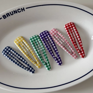 Detail of six colorful checkered BB hair clips in a ceramic tray with soft lighting