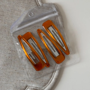 Detail of four amber orange triangular BB clips with marble texture in transparent bag