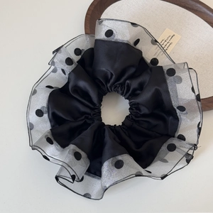 Detail of a large black satin scrunchie featuring elegant polka dot tulle ruffled edges
