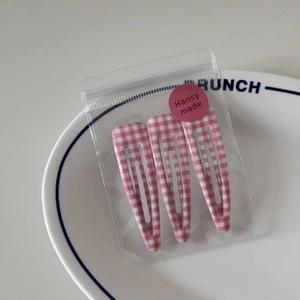 Detailed view of pink gingham BB hair clips set in branded transparent zip packaging