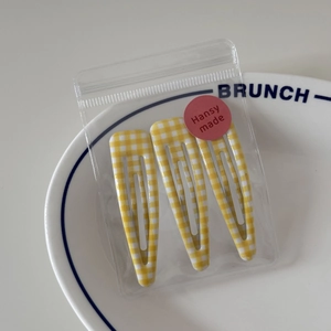 Detailed view of three yellow gingham print BB hair clips displayed on a white ceramic plate