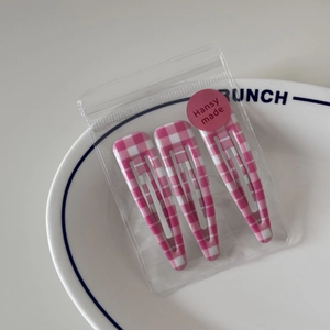 Detail of three pink gingham BB hair clips in transparent packaging on a white ceramic plate