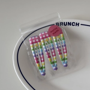 Close-up of three checkered BB hair clips in a branded bag on a white ceramic plate
