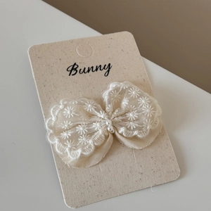Detailed macro view of an off-white lace bow hair clip with embroidery and small pearls