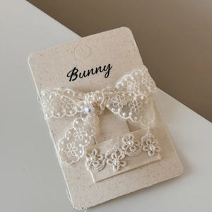 Detail of cream lace bow hair clips with faux pearls on premium paper card