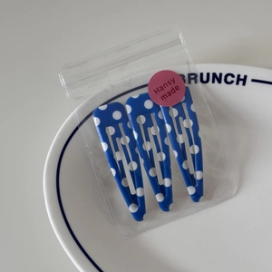 Detail of three blue polka dot snap hair clips displayed on a white ceramic brunch plate