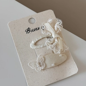 Close-up of off-white lace bow hair clip and pearl ribbon barrette set on card
