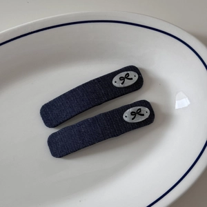 Détail de deux barrettes en denim bleu foncé avec motifs de nœuds blancs sur une assiette