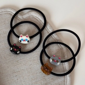 Detail of four cartoon cat hair ties in black, white, grey, and brown on a linen heart pad