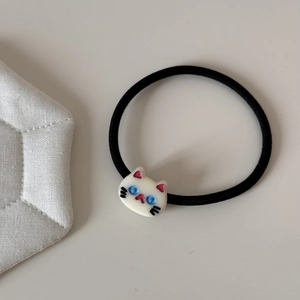 Close-up of cute cream cat charm with blue eyes on high-elastic black hair tie