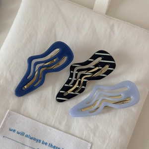 Détail de trois barrettes à cheveux ondulées en acétate bleu, lavande et rayé