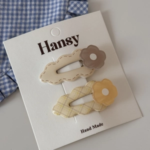 Two-piece set of beige and yellow wavy flower hair clips on a white display card