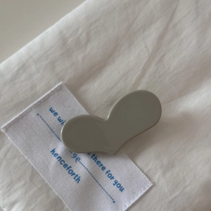 Gros plan d'une pince à cheveux minimaliste en forme de cœur gris sur tissu blanc