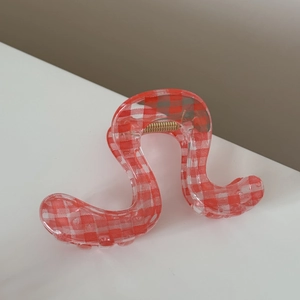 Detail of wavy hair claw clip with classic red and white gingham pattern and gold spring