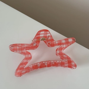 Close-up of a star-shaped red and white plaid hair claw clip with golden metal spring