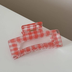 Close-up of a red and white gingham checkered hair claw clip with golden metal spring